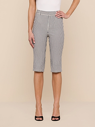 A person stands against a plain background, showcasing the lower half of their body dressed in the Leni Pedal Pusher—black and white vertically striped cotton seersucker knee-length shorts—paired with a sleeveless white top and black open-toe heels.
