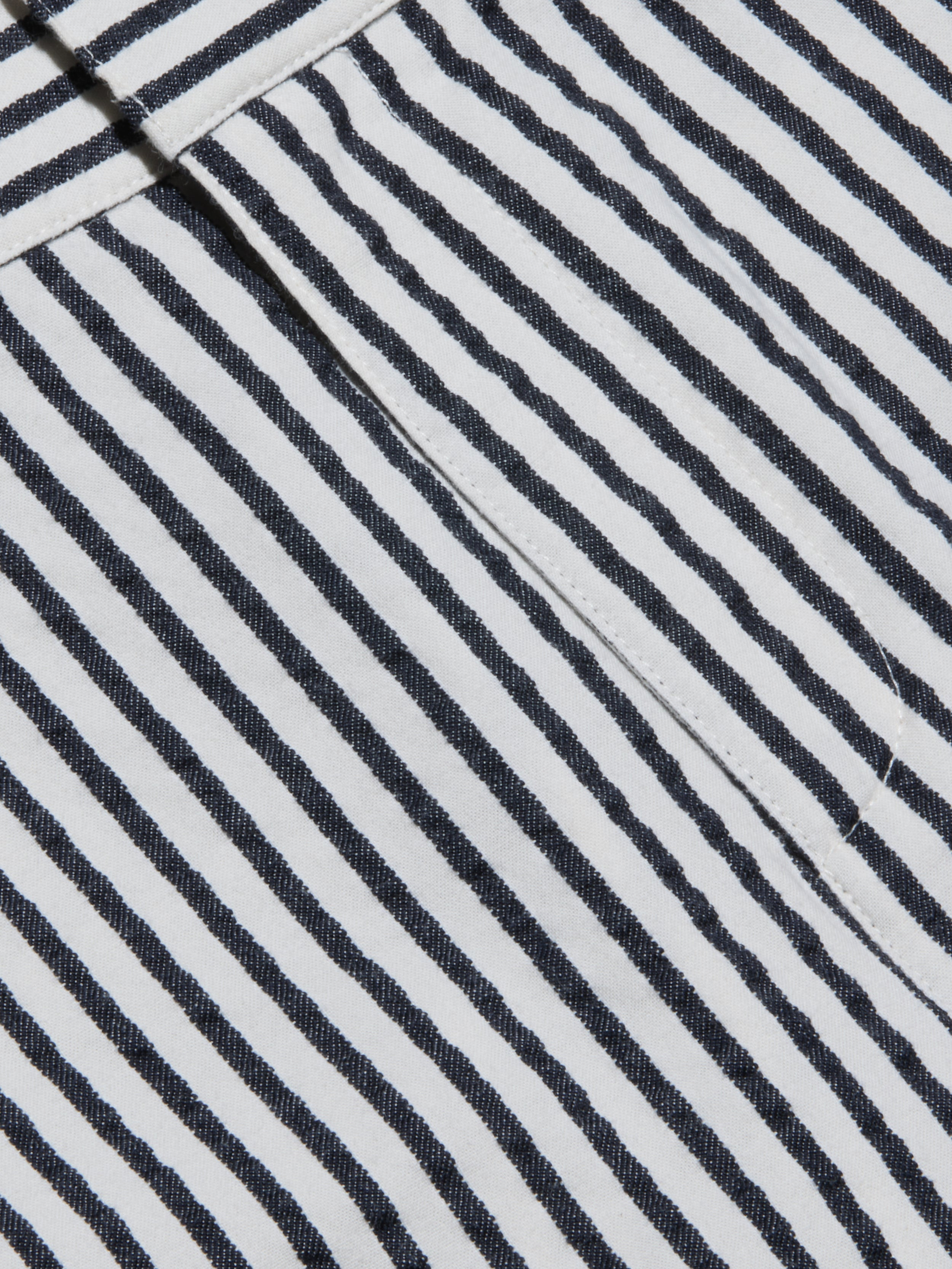 Close-up of the Leni Pedal Pusher’s black and white vertical striped cotton seersucker fabric, showcasing a visible seam and a folded edge that highlight its textured, patterned appearance.
