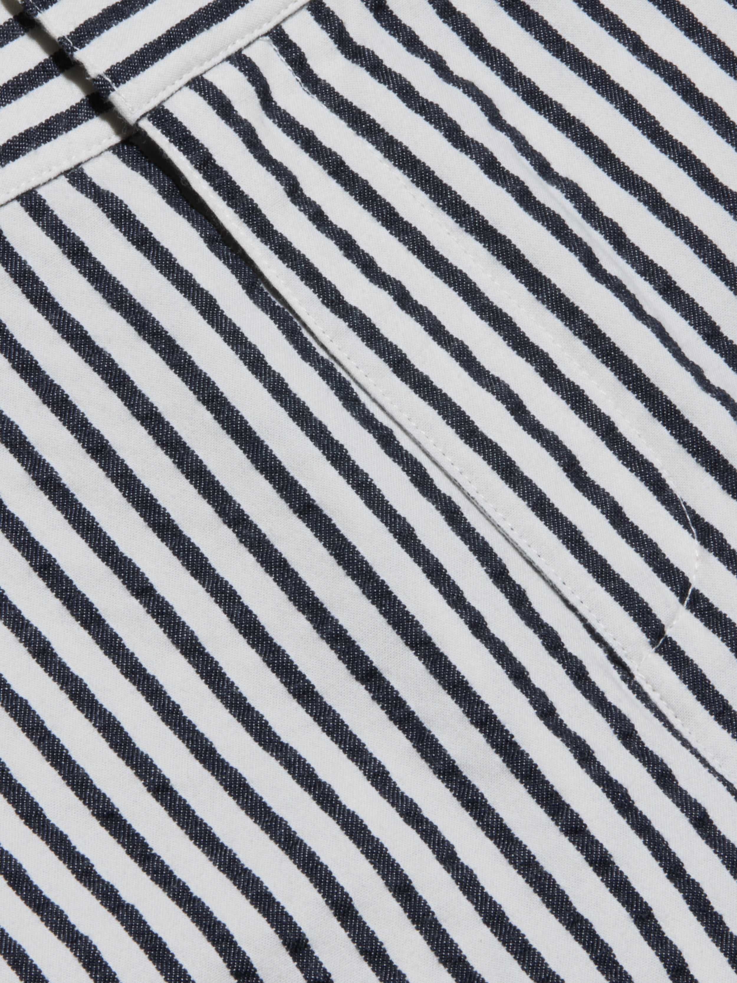 Close-up of the Leni Pedal Pusher’s black and white vertical striped cotton seersucker fabric, showcasing a visible seam and a folded edge that highlight its textured, patterned appearance.