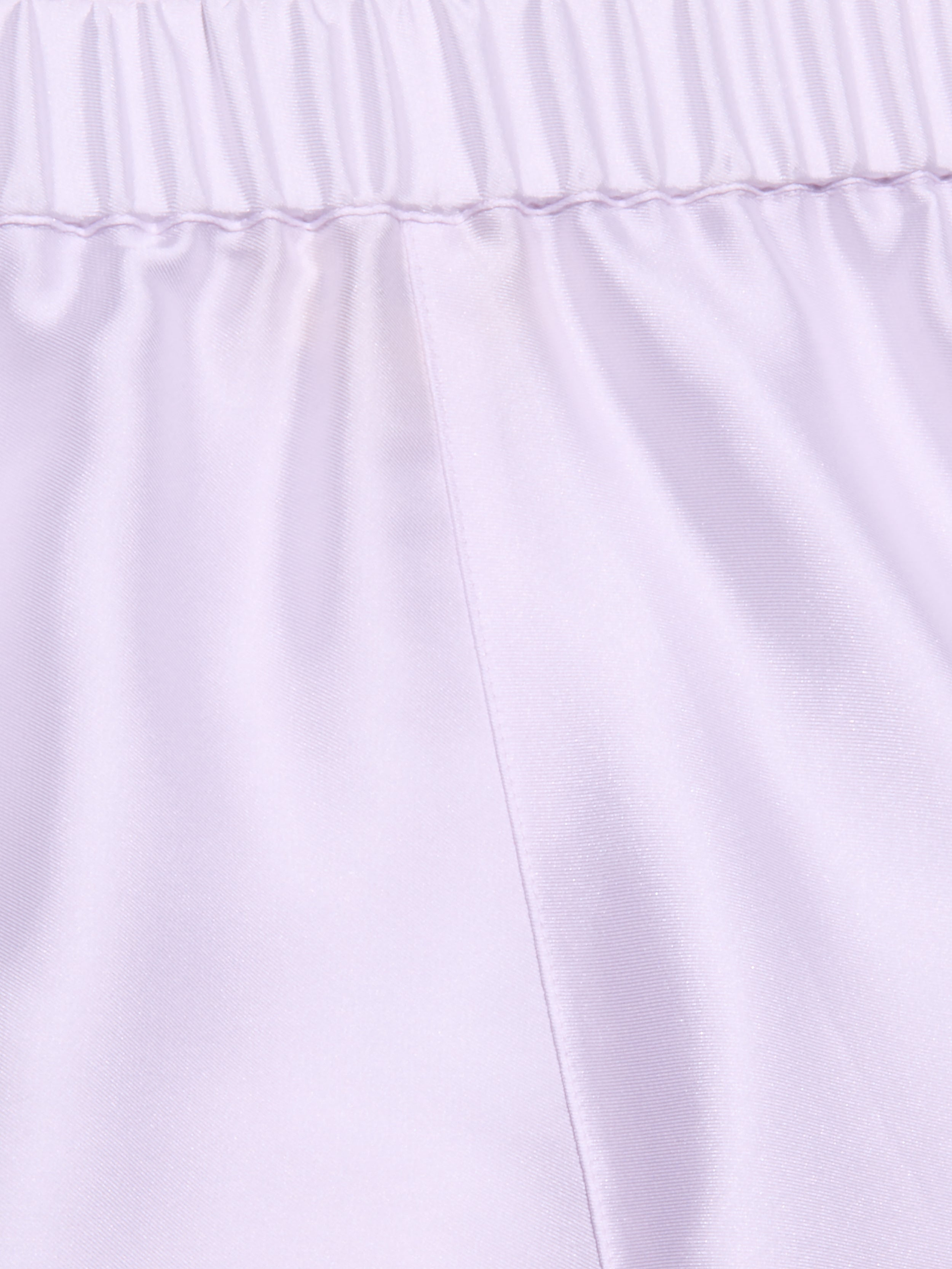 Close-up of the Maela Short in light purple, featuring a shiny poly twill fabric, an elastic waistband, and a visible vertical center seam—ideal for comfortable pull-on wear.