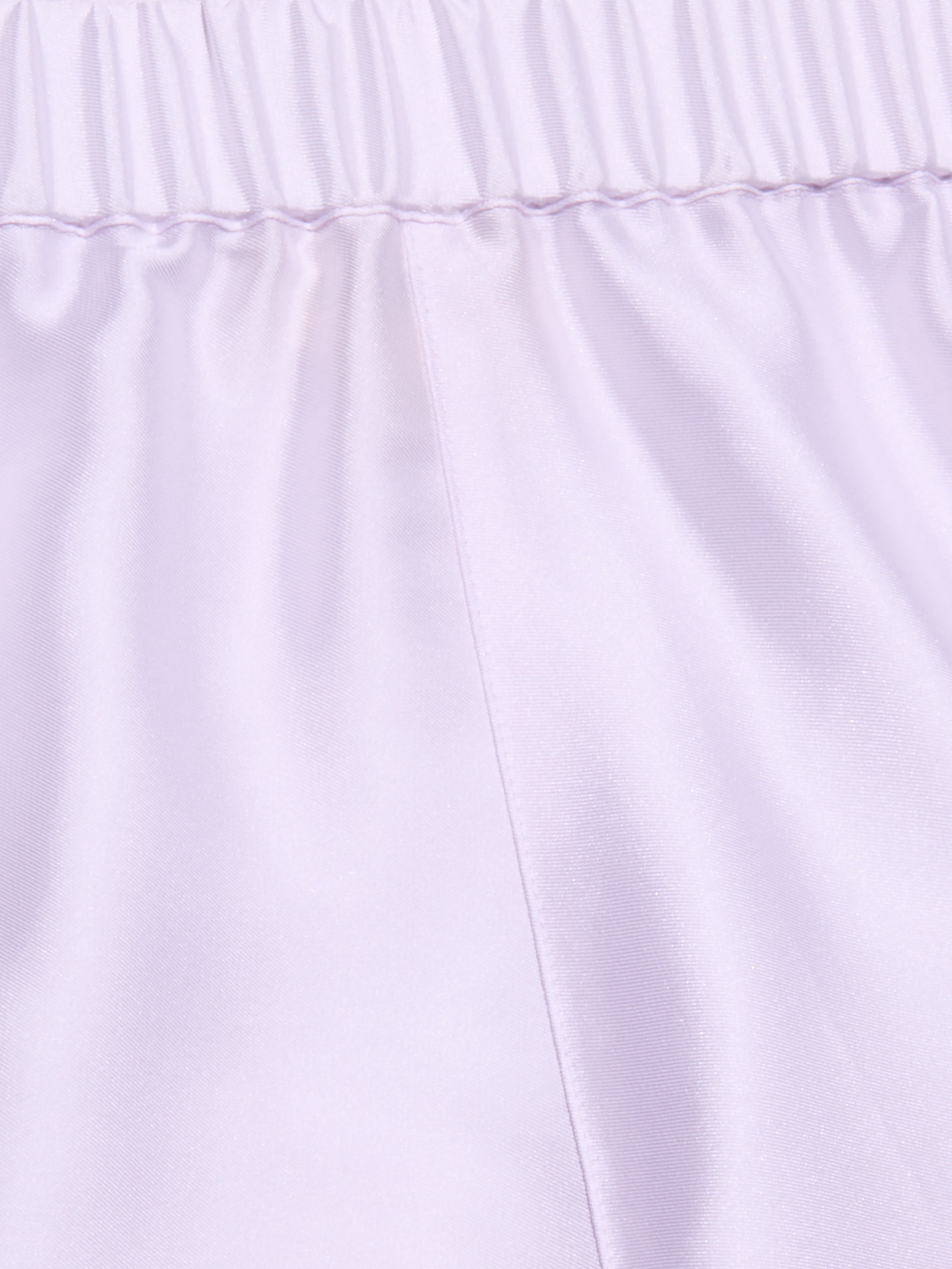 Close-up of the Maela Short in light purple, featuring a shiny poly twill fabric, an elastic waistband, and a visible vertical center seam—ideal for comfortable pull-on wear.