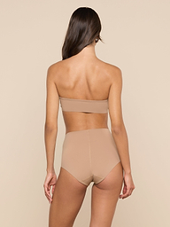 A woman with long brown hair, seen from behind, wears a strapless nude bandeau bra and the Velle Knit Panty against a plain white background.