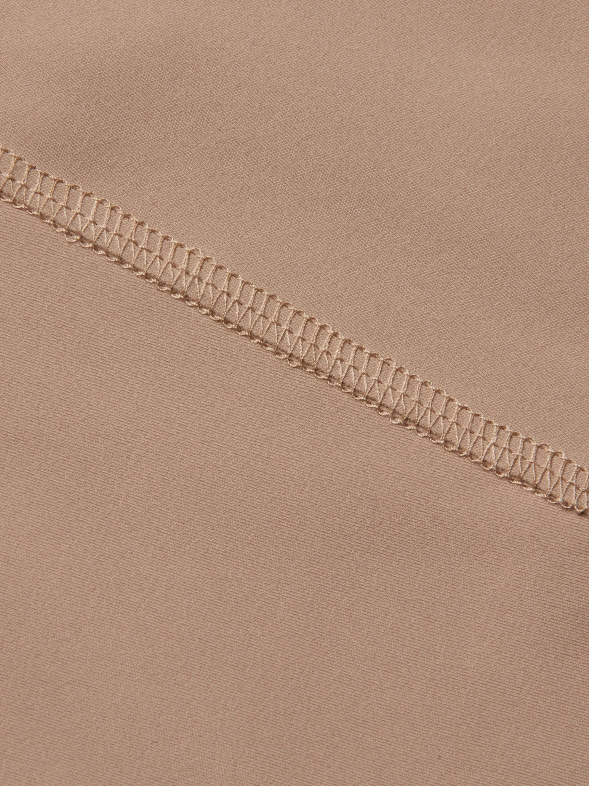 Close-up of beige fabric from the Velle Knit Panty, featuring a high waist design with a visible overlock stitch seam running diagonally, highlighting the intricate threadwork and smooth textile texture.