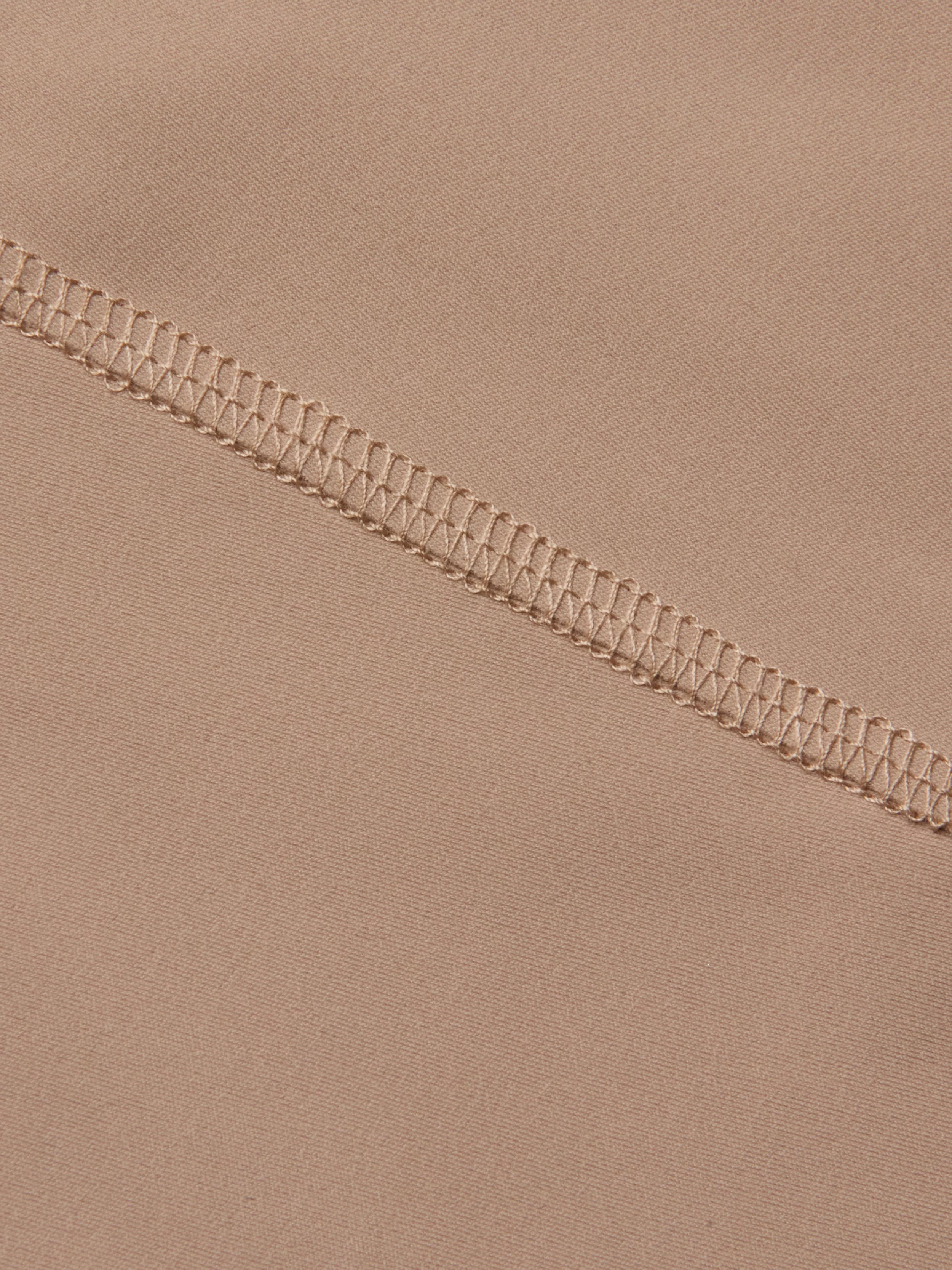 Close-up of beige fabric from the Velle Knit Panty, featuring a high waist design with a visible overlock stitch seam running diagonally, highlighting the intricate threadwork and smooth textile texture.
