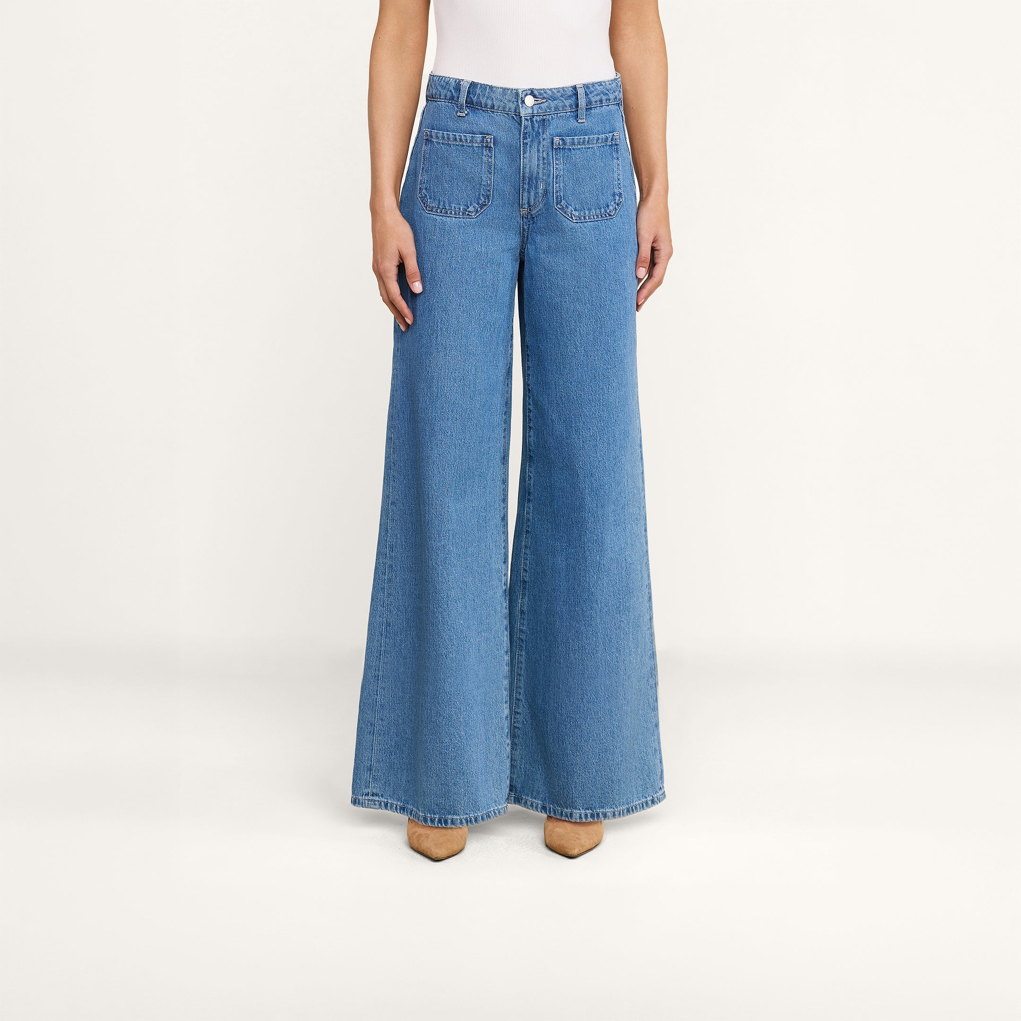 Une personne se tient debout, les bras le long du corps, vêtue du jean à jambes larges Delcan, à taille haute et doté de poches plaquées sur le devant, sur un fond beige uni.