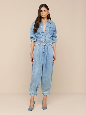 Une femme aux cheveux longs et lâchés et à lexpression neutre se tient sur un fond beige, vêtue dune chemise en denim bleu clair, de talons bleus et du jean à jambe large Elias. Le jean est un modèle palazzo à taille haute et à jambe large.