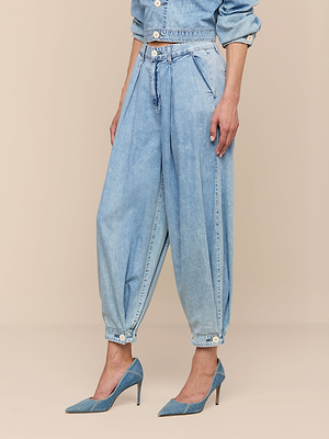 Une personne portant le jean à jambes larges Elias - un jean palazzo plissé, à taille haute et poids plume, avec des chevilles boutonnées - associé à des talons en denim assortis et à une chemise en denim à manches longues rentrée dans le pantalon, pour un look de transition parfait.