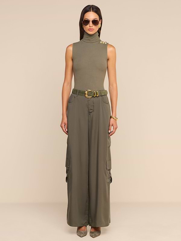 A woman wearing sunglasses, a sleeveless olive green turtleneck top, the Isolde Cargo Pant crafted from lightweight Tencel, a belt, and heels stands against a plain white background.
