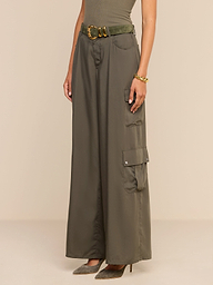 A woman is shown from the shoulders down, standing against a plain white background. She wears the Isolde Cargo Pant in wide-leg olive green tencel with a matching belt, paired with a sleeveless top, a bracelet, and taupe high heels.