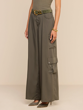 A person wearing the Isolde Cargo Pant in olive green, featuring wide legs, lightweight tencel fabric, and a matching belt, styled with a sleeveless top and pointed heels. Only the lower half of their body is visible.