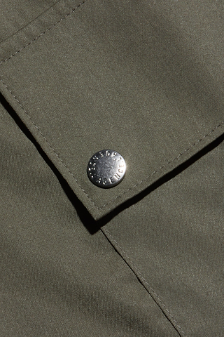 Close-up of an olive green lightweight tencel fabric on the Isolde Cargo Pant, showcasing a neatly stitched flap with a metallic rivet button embossed with text—a refined detail characteristic of modern cargo pant designs.