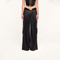 Wearing the Isolde Cargo Pant—black wide-leg vegan leather pants with utility pockets and a belt featuring a yellow buckle—paired with a matching cropped black vest, this person stands against a plain white background with their face out of frame.