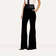 A person wearing the Prudence Cummerbund Trouser—high rise, wide-leg black pants—paired with a white top. Their left hand rests in their pocket as they stand against a plain light background, with their face not visible.
