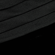 Close-up of the Prudence Cummerbund Trouser in black velvet, featuring diagonal, slightly curved folds. The soft and smooth texture is highlighted by subtle shadows and highlights that accentuate the contours of the pleats.