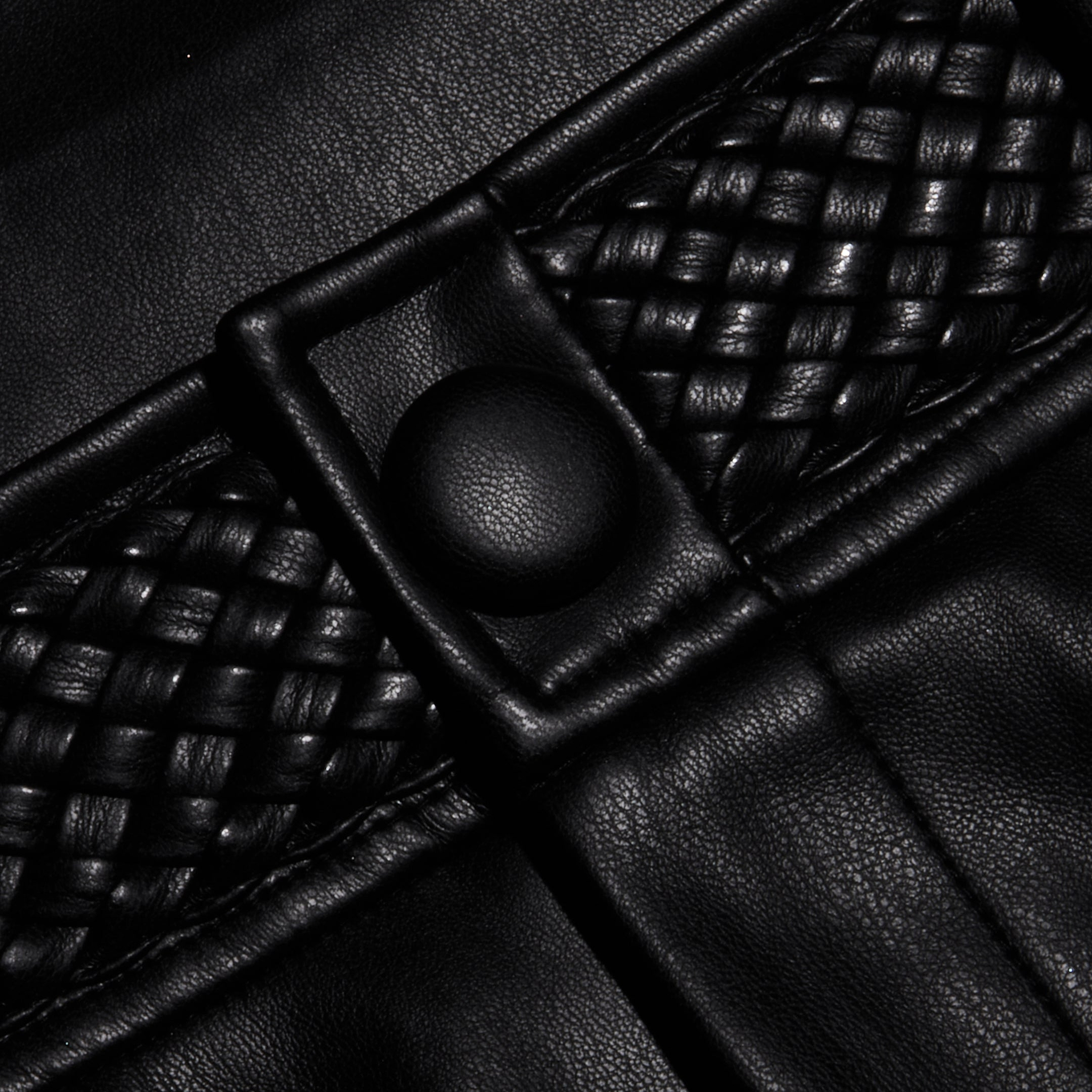 Close-up of the Virelle Short in black vegan leather, showcasing woven detailing and a round button. The texture and stitching are clearly visible, highlighting the striking contrast between smooth and braided sections—perfectly reflecting the quality finish of these high rise vegan leather shorts.
