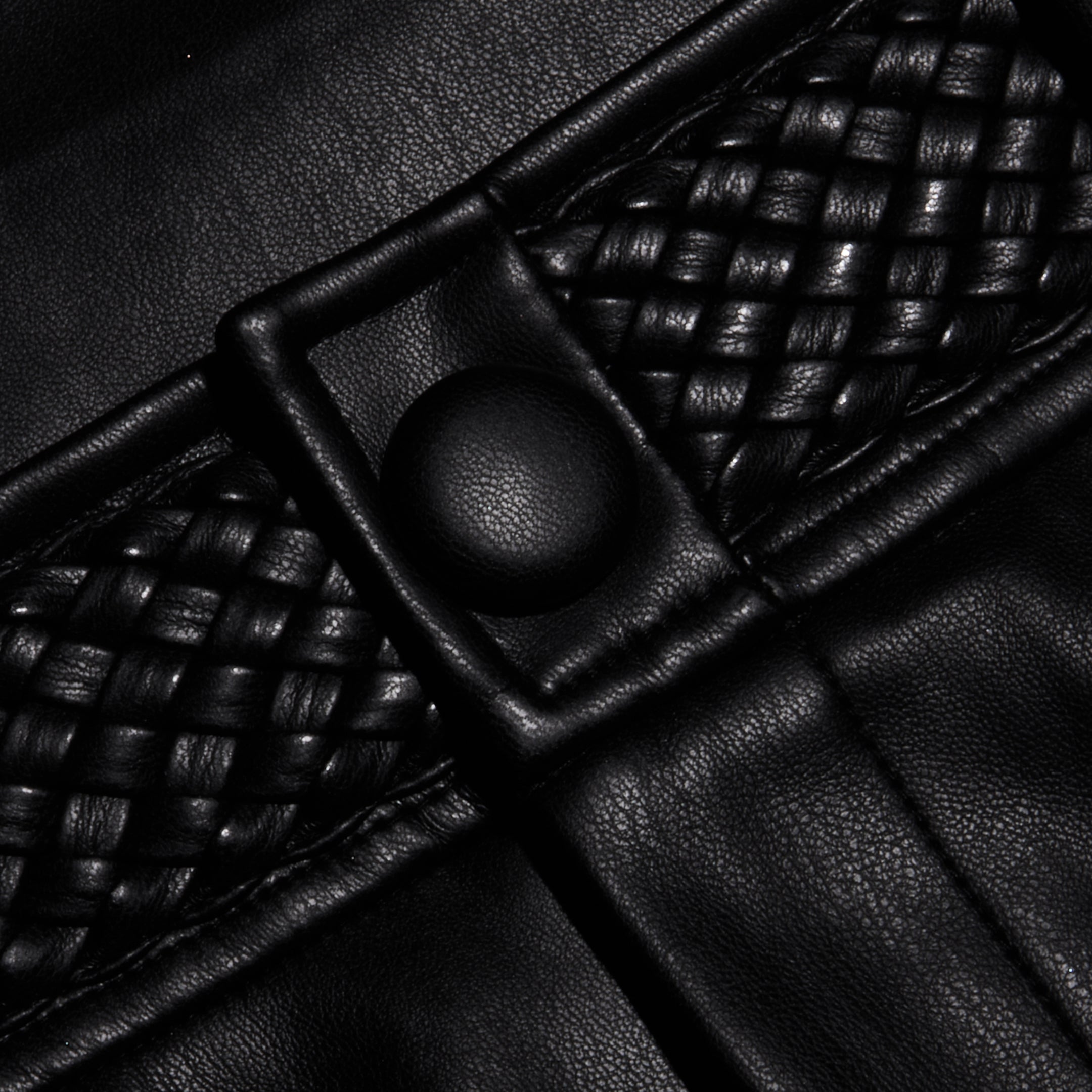 Close-up of the Virelle Short in black vegan leather, showcasing woven detailing and a round button. The texture and stitching are clearly visible, highlighting the striking contrast between smooth and braided sections—perfectly reflecting the quality finish of these high rise vegan leather shorts.