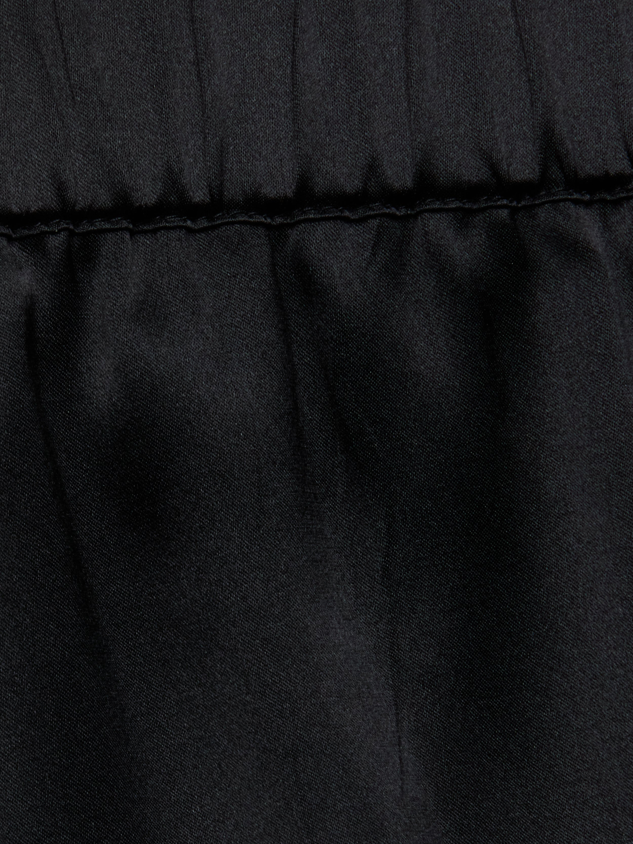 Close-up of the Joy Silk Lace Short in black, featuring a horizontal stitched seam near the top. The fabric above the seam is slightly gathered, forming soft folds and showcasing a smooth, matte texture—perfect for warm-weather style.