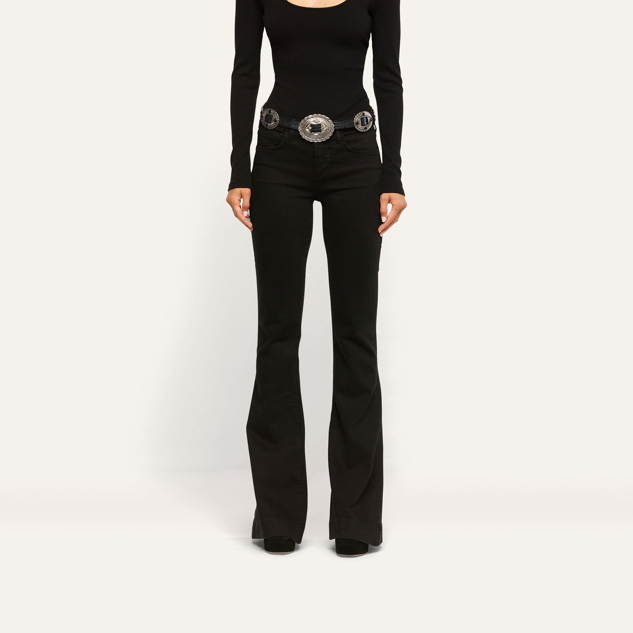 Her Story Flare Jean in black, low-rise, slim-cut, worn with a long-sleeved black top and a silver western-style belt.