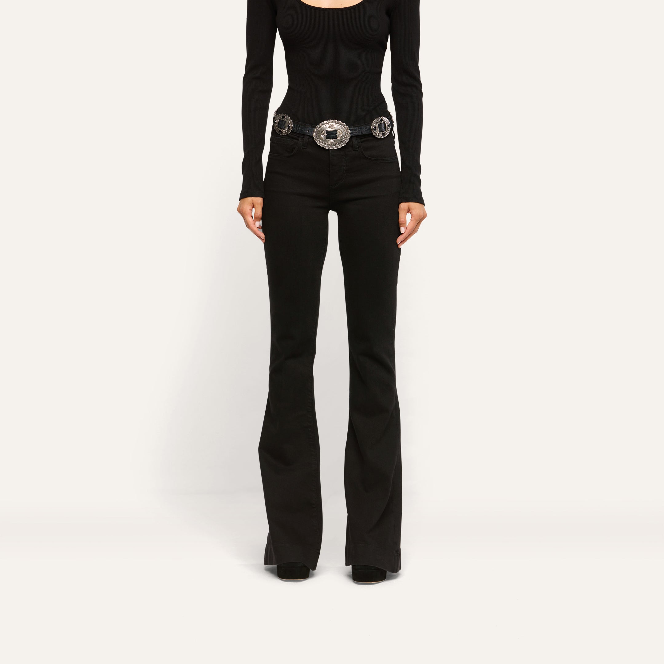 Her Story Flare Jean in black, low-rise, slim-cut, worn with a long-sleeved black top and a silver western-style belt.