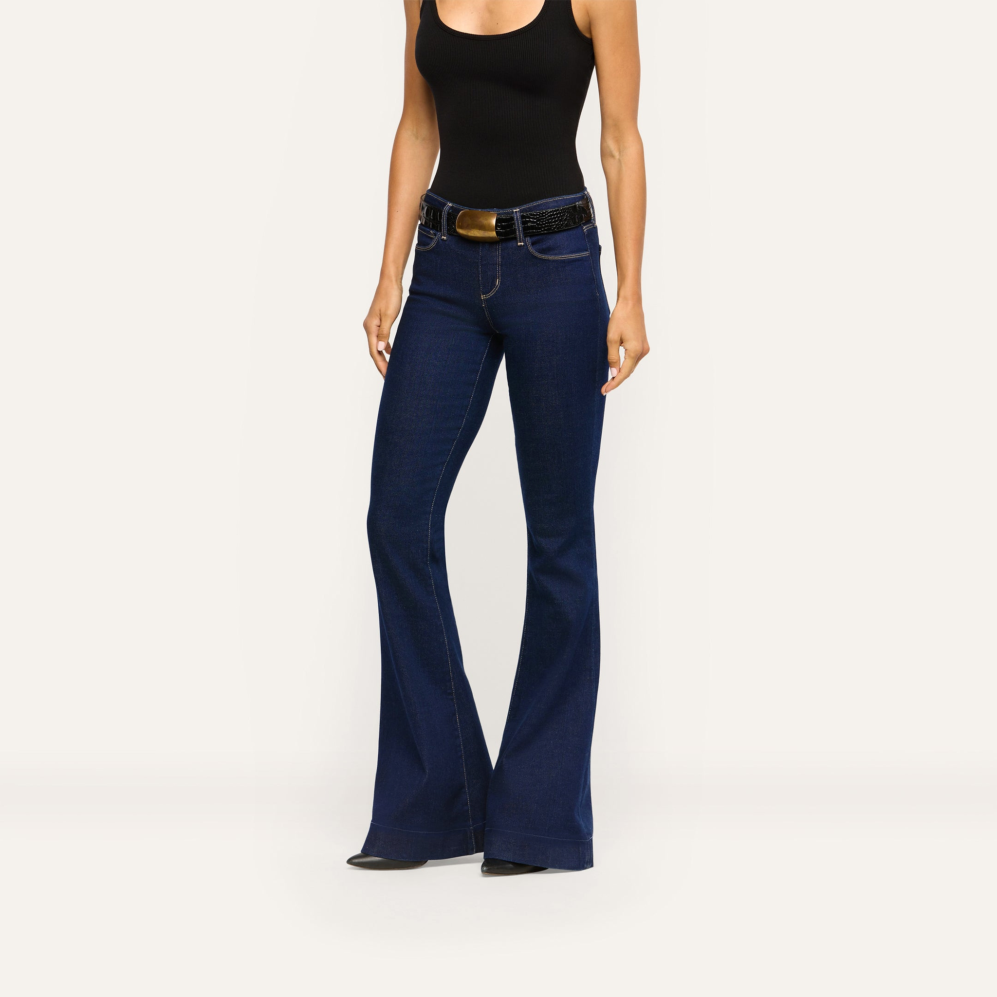 Her Story Flare Jean in dark indigo slim-cut denim worn with a black tank top and a black textured belt with a gold buckle.