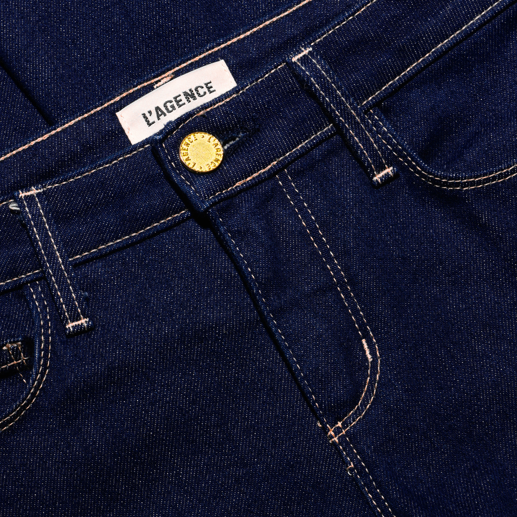 Close-up of dark indigo, low-rise Her Story Flare Jean featuring a gold-tone button fly and a white brand label at the waistband.