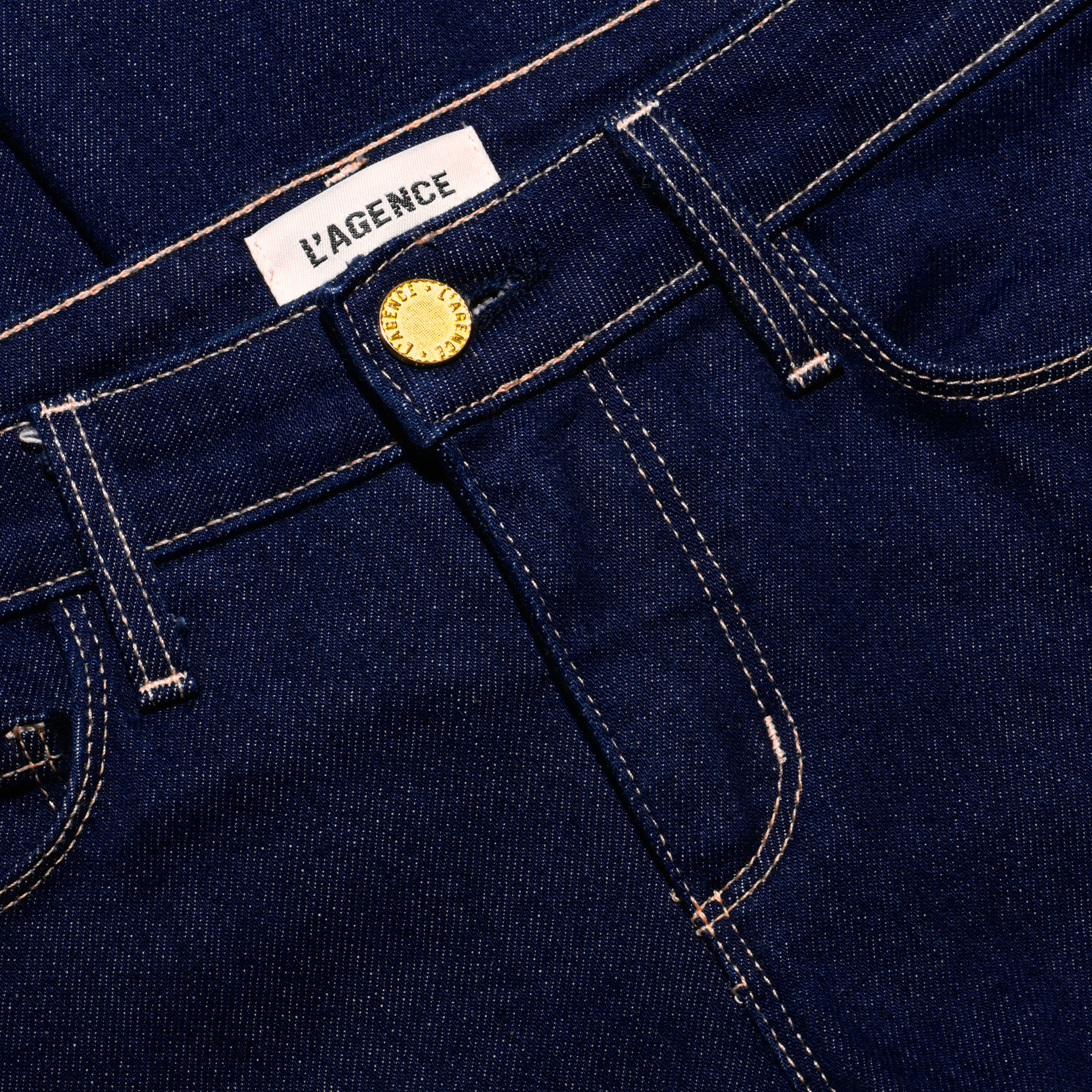 Close-up of dark indigo, low-rise Her Story Flare Jean featuring a gold-tone button fly and a white brand label at the waistband.