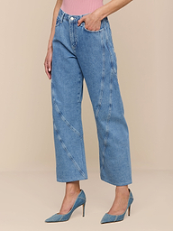 Portant le Frasier Rodeo Jean en denim bleu haut avec des coutures décoratives, un haut rose et des talons bleus à bouts pointus, une personne se tient debout sur un fond beige uni.