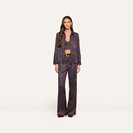 A woman with long brown hair and a neutral expression stands against a plain background, wearing the Livvy Trouser in a matching midnight paisley print, paired with a long-sleeved button-up shirt and a visible bralette underneath.