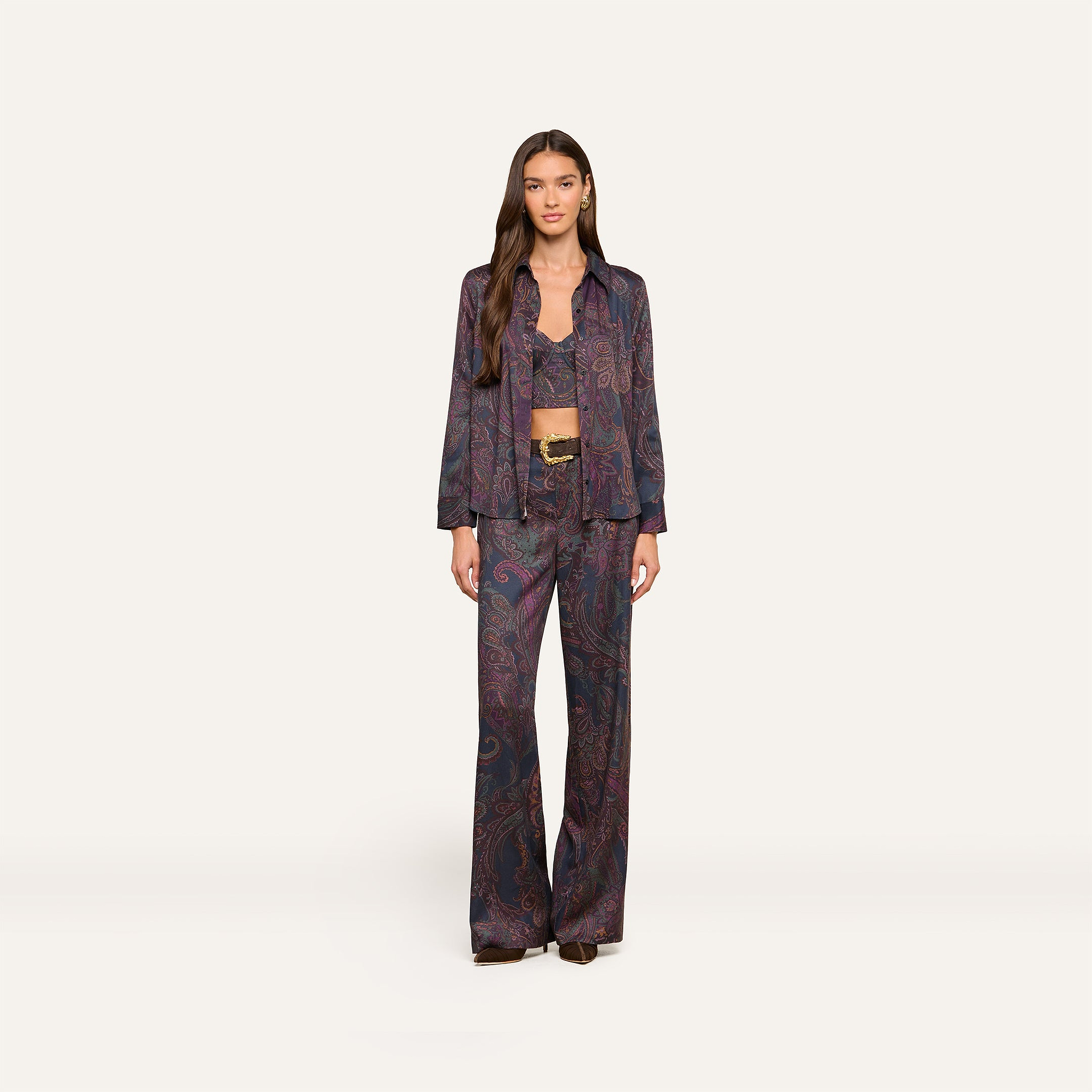 A woman with long brown hair and a neutral expression stands against a plain background, wearing the Livvy Trouser in a matching midnight paisley print, paired with a long-sleeved button-up shirt and a visible bralette underneath.