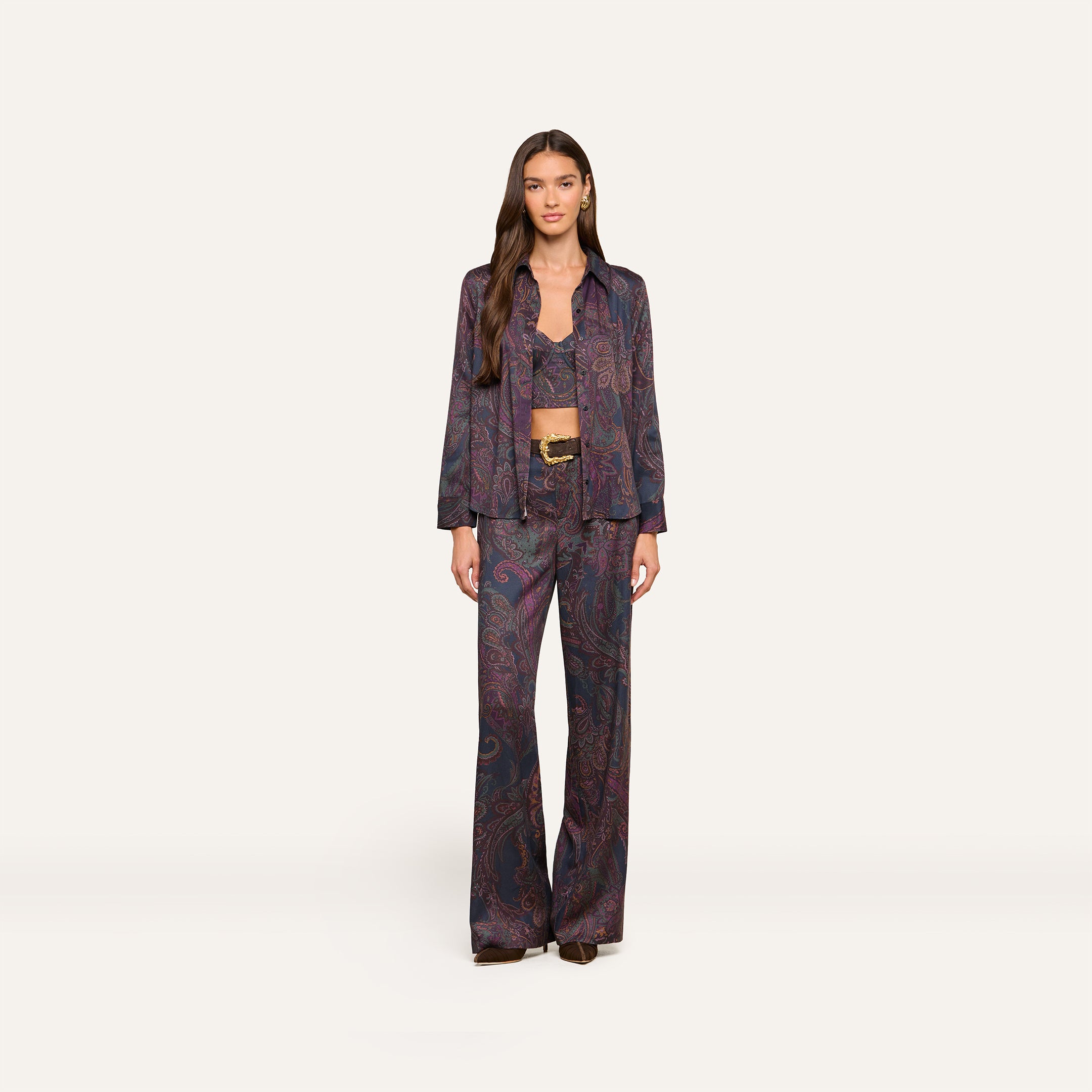A woman with long brown hair and a neutral expression stands against a plain background, wearing the Livvy Trouser in a matching midnight paisley print, paired with a long-sleeved button-up shirt and a visible bralette underneath.