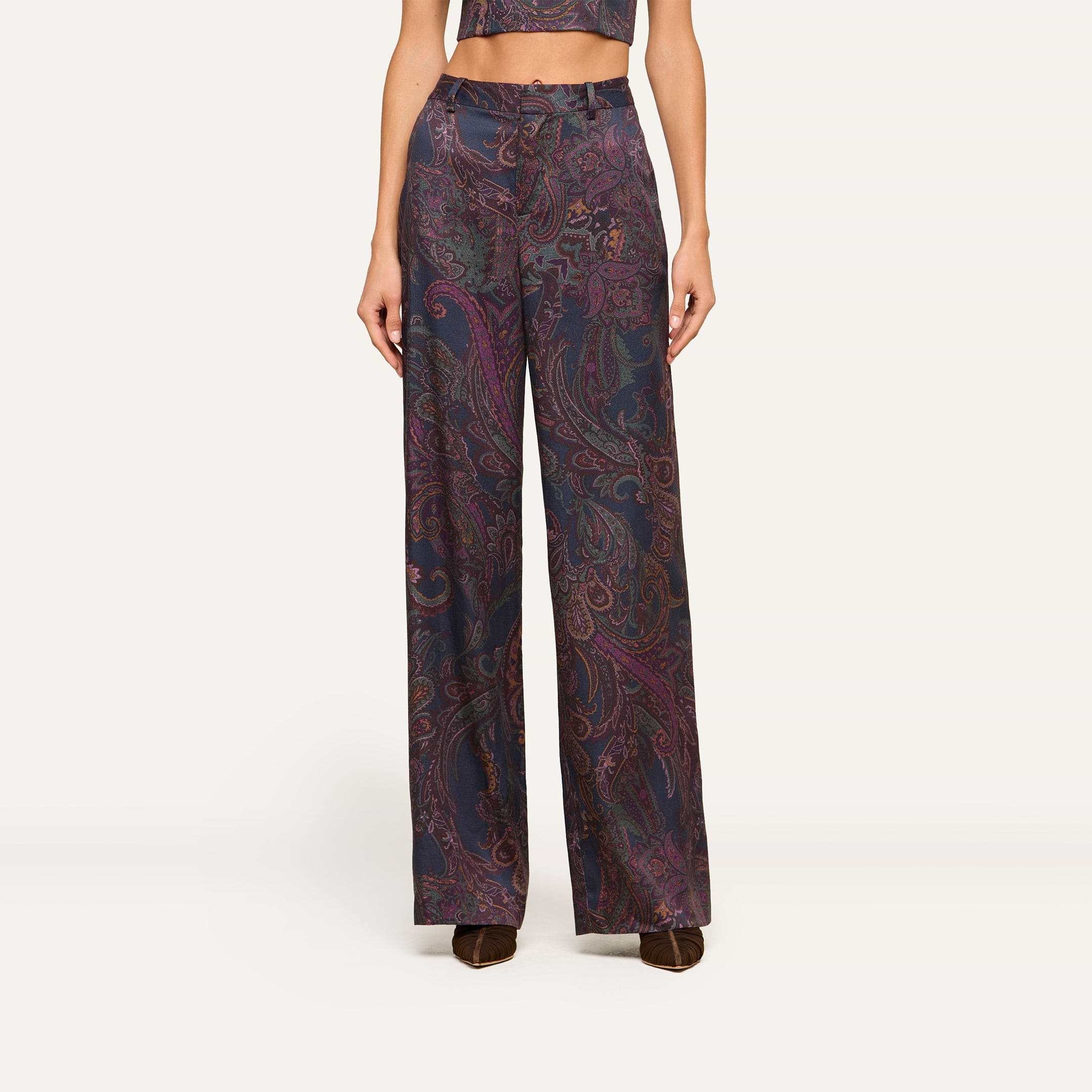 Wearing the Livvy Trouser—a high-rise, wide-leg pant in a dark midnight paisley print—paired with the matching cropped top and brown shoes, this person stands against a plain light background.