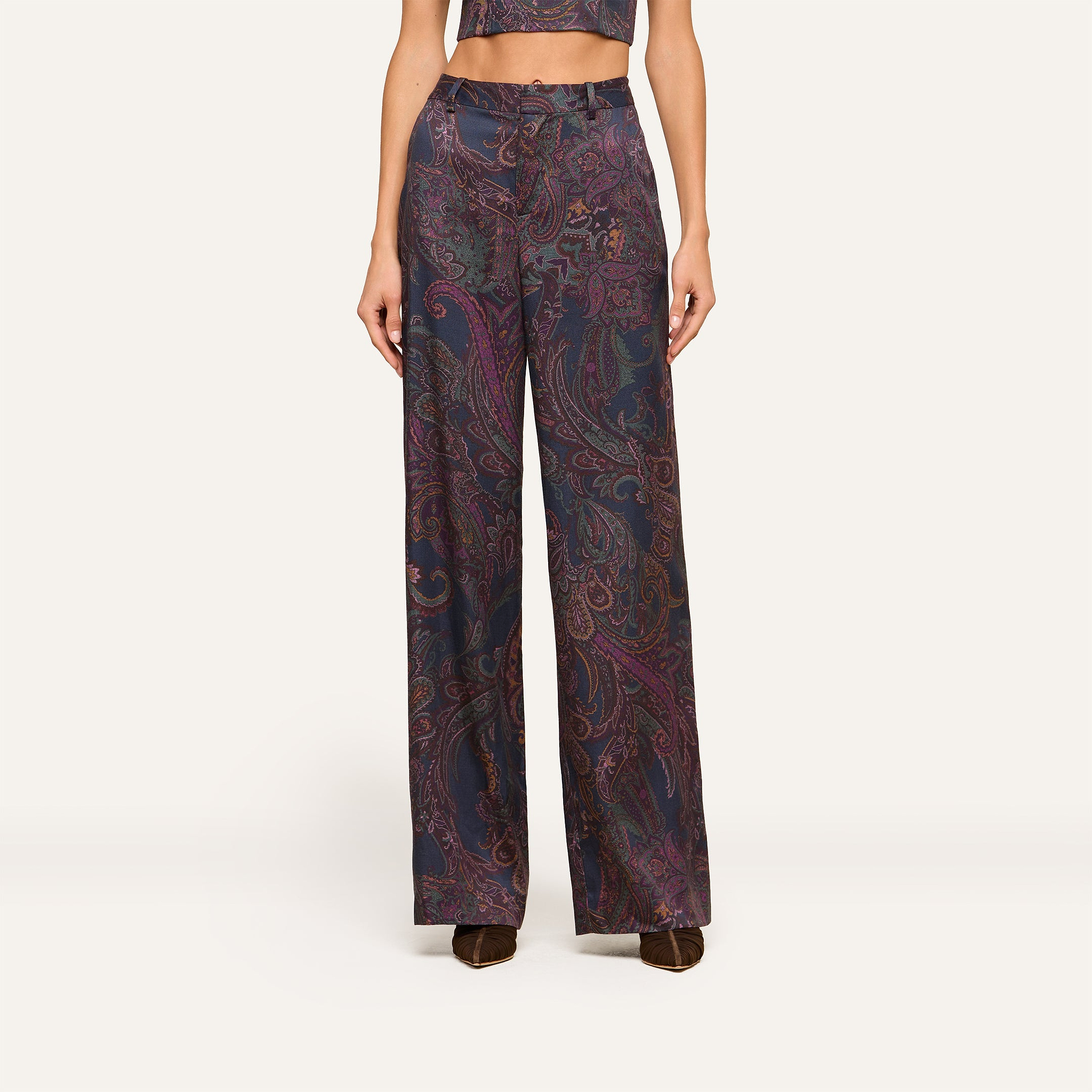 Wearing the Livvy Trouser—a high-rise, wide-leg pant in a dark midnight paisley print—paired with the matching cropped top and brown shoes, this person stands against a plain light background.