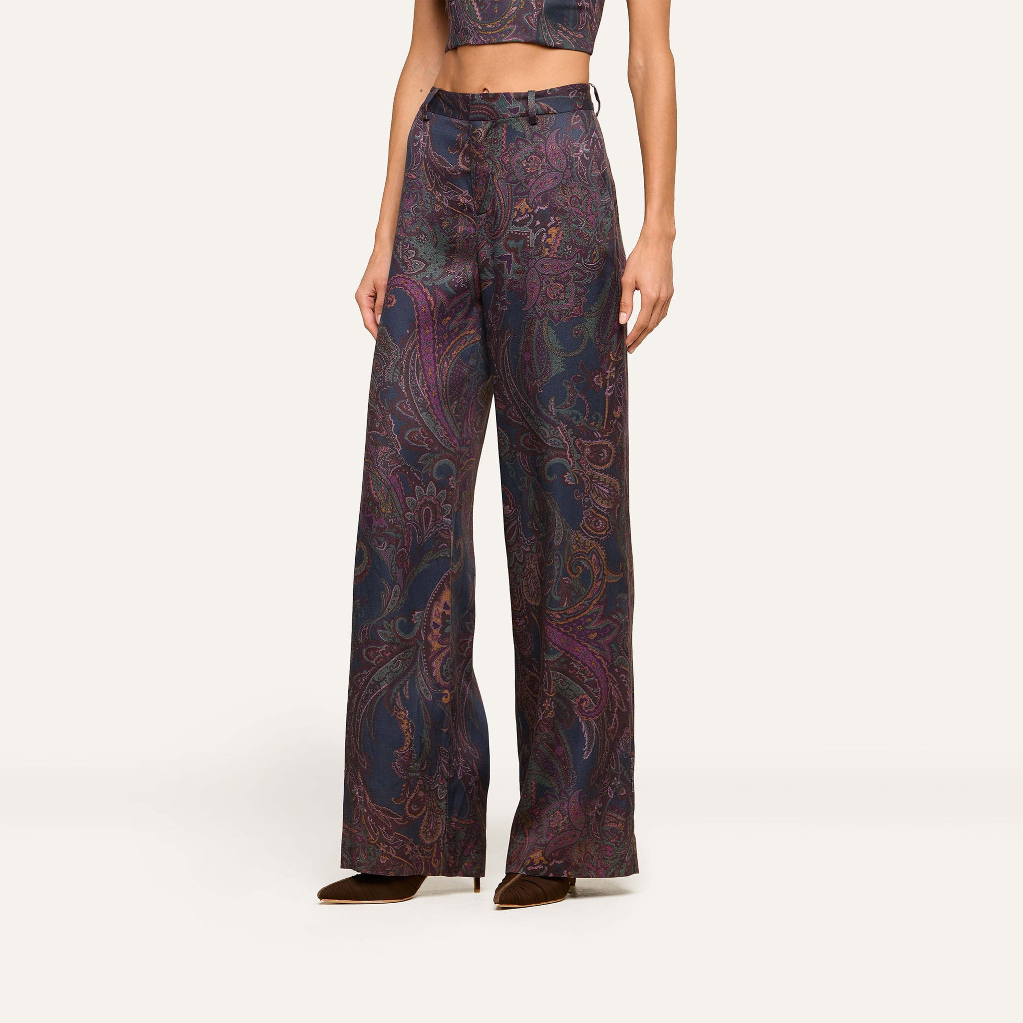 A person wearing the Livvy Trouser, a high-rise, wide-leg pant featuring a midnight paisley print in dark shades, paired with a matching crop top and shown from the shoulders down against a plain background.