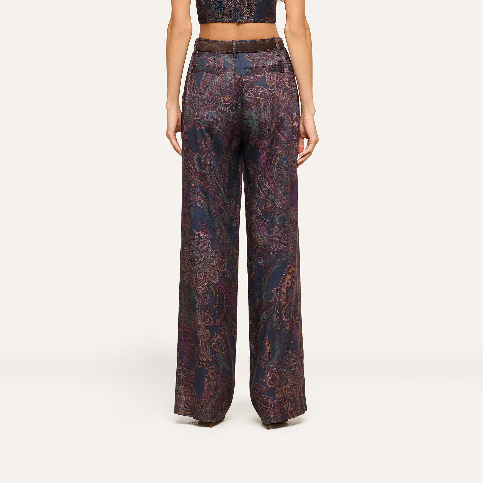 A person wearing the Livvy Trouser, a high-rise, wide-leg pant in midnight paisley, paired with a matching cropped top and shown from the back against a plain background.