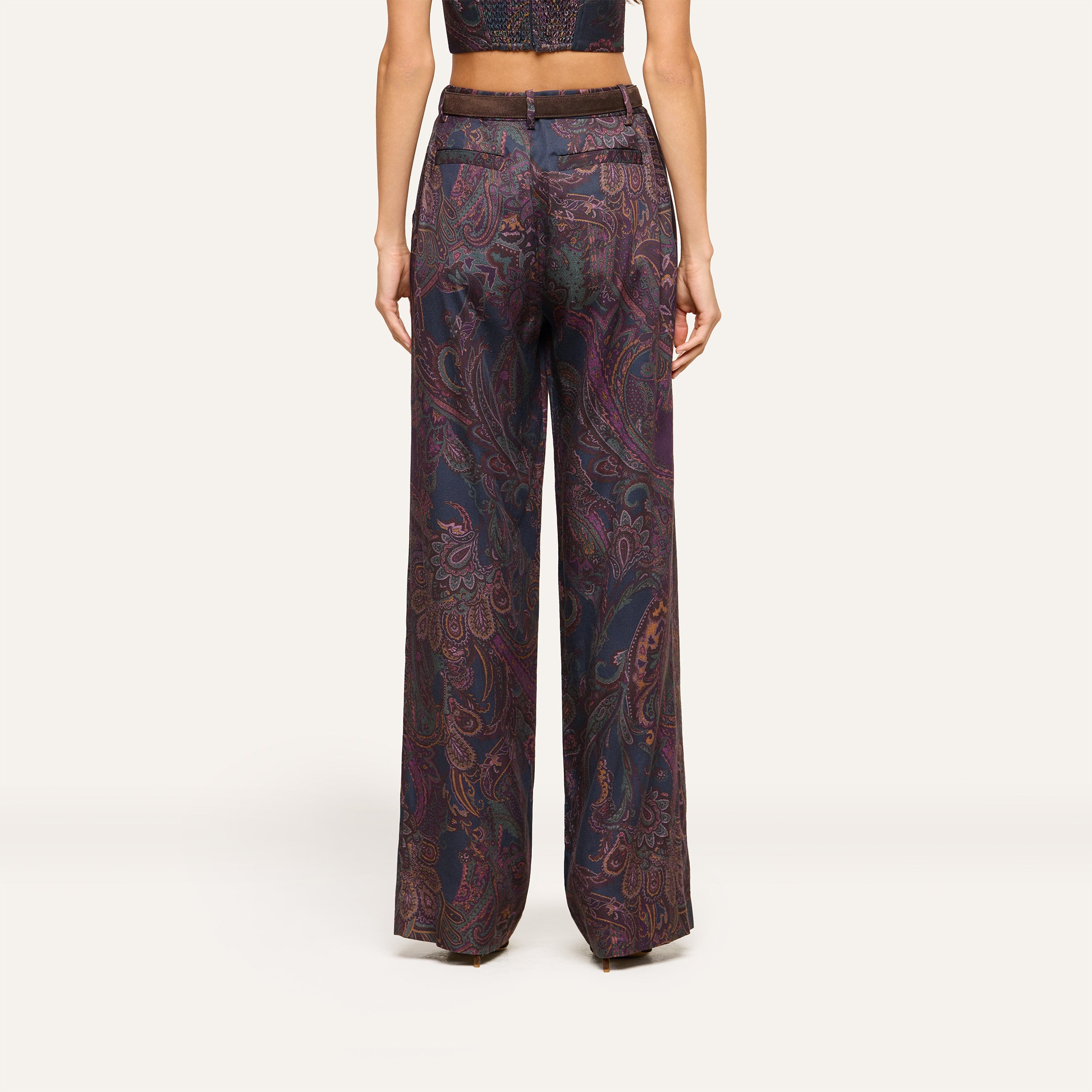 A person wearing the Livvy Trouser, a high-rise, wide-leg pant in midnight paisley, paired with a matching cropped top and shown from the back against a plain background.