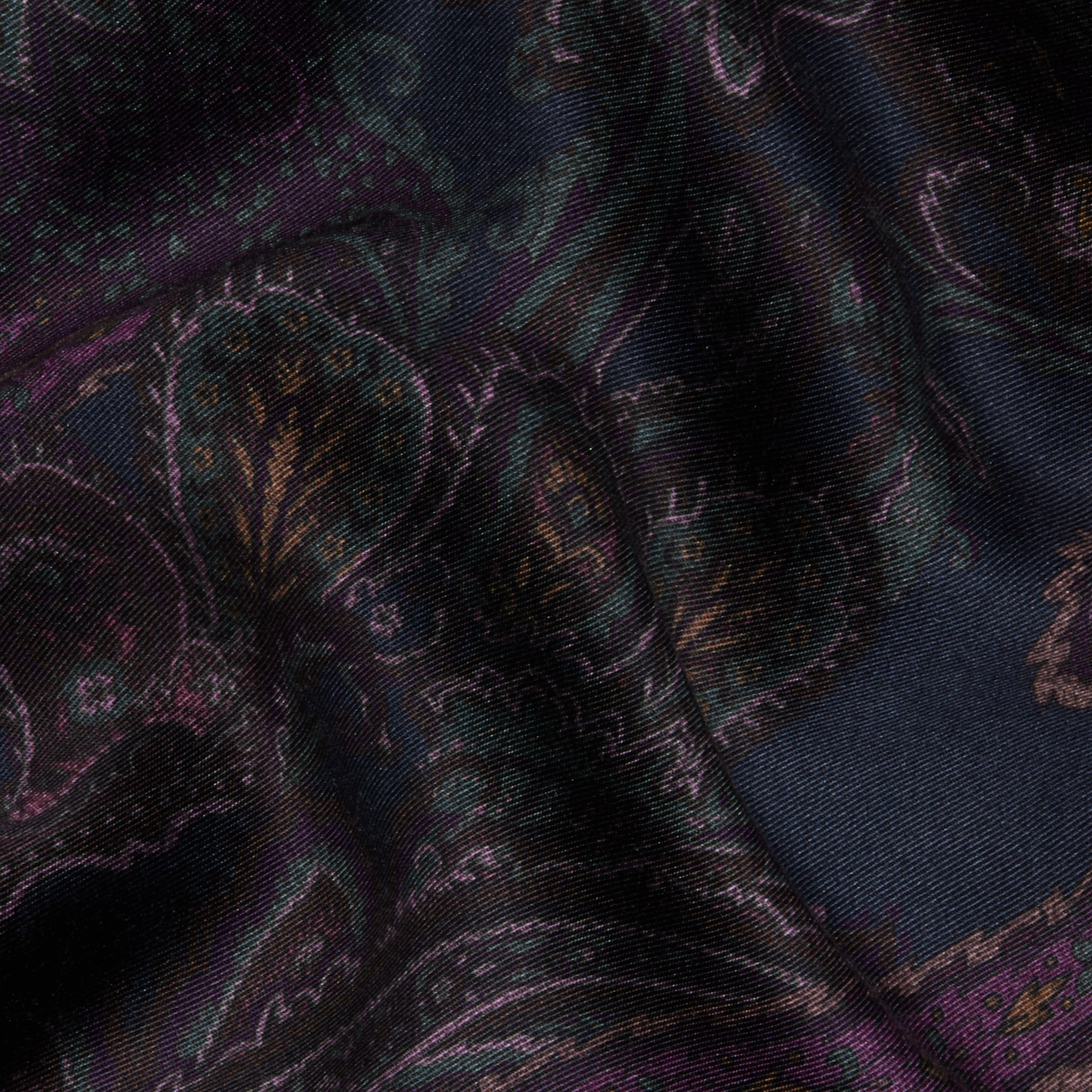 The Livvy Trouser features a dark, richly patterned fabric adorned with a midnight paisley design in shades of purple, green, and gold; the material appears slightly wrinkled and is softly illuminated.