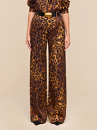 A person wearing the Livvy Trouser—a high-waisted, straight-leg style in tan leopard print—paired with a black belt featuring a large gold buckle, stands against a plain white background.