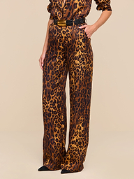 A person is shown wearing the Livvy Trouser, a tan leopard print jumpsuit featuring wide, straight-leg trousers and a black belt, standing against a plain white background with their face not visible.