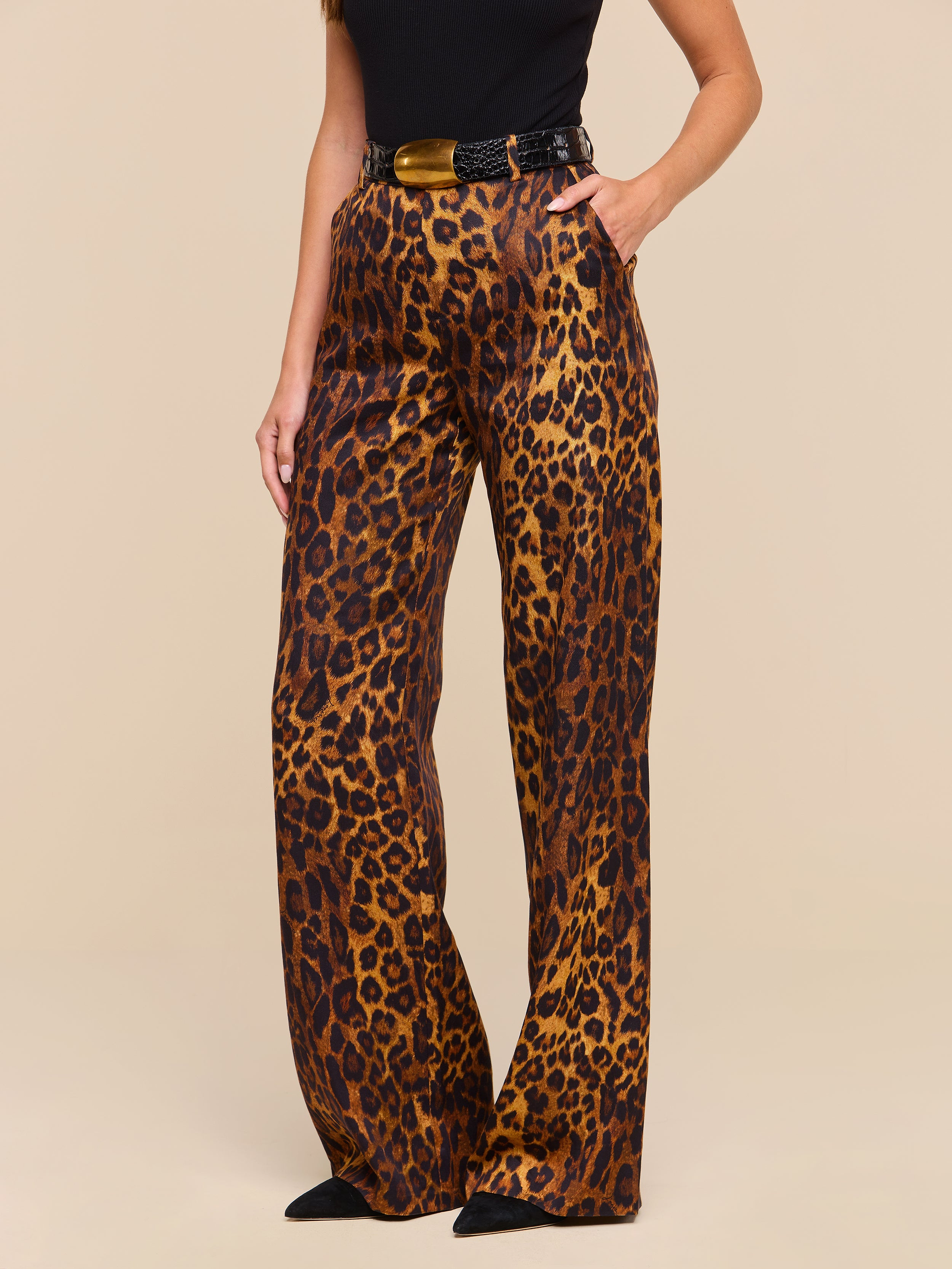 A woman is shown from torso to feet wearing the Livvy Trouser, which features a high-waisted, wide-leg silhouette in tan leopard print, paired with a black top and pointed black shoes against a plain background.