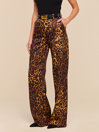 A woman stands with one hand in her pocket, wearing the Livvy Trouser—high-waisted, straight-leg tan leopard print trousers crafted from printed twill—styled with a black belt and a black sleeveless top.