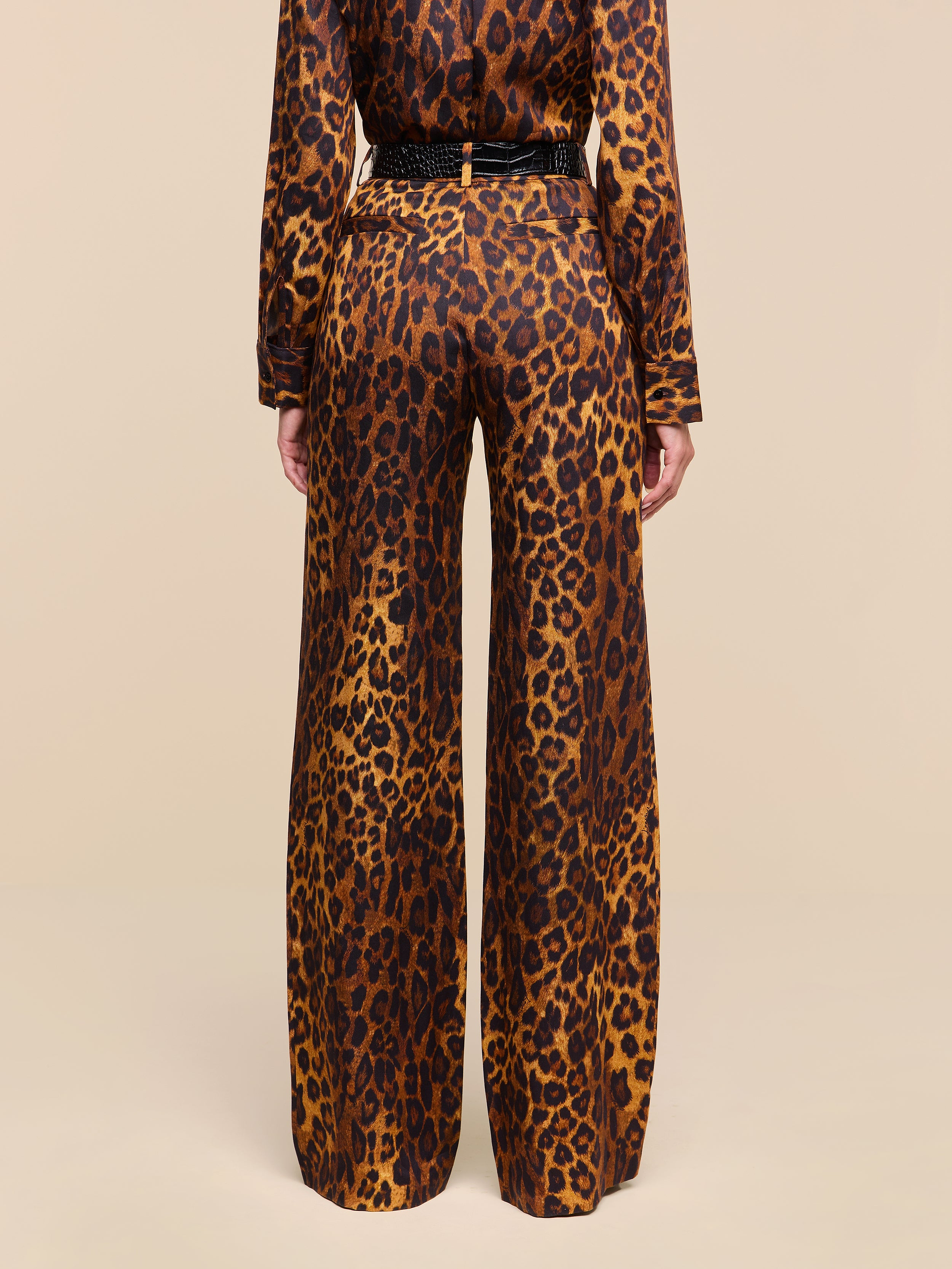 A person stands with their back to the camera, wearing the Livvy Trouser and a matching long-sleeve top in a tan leopard print pattern against a plain white background.