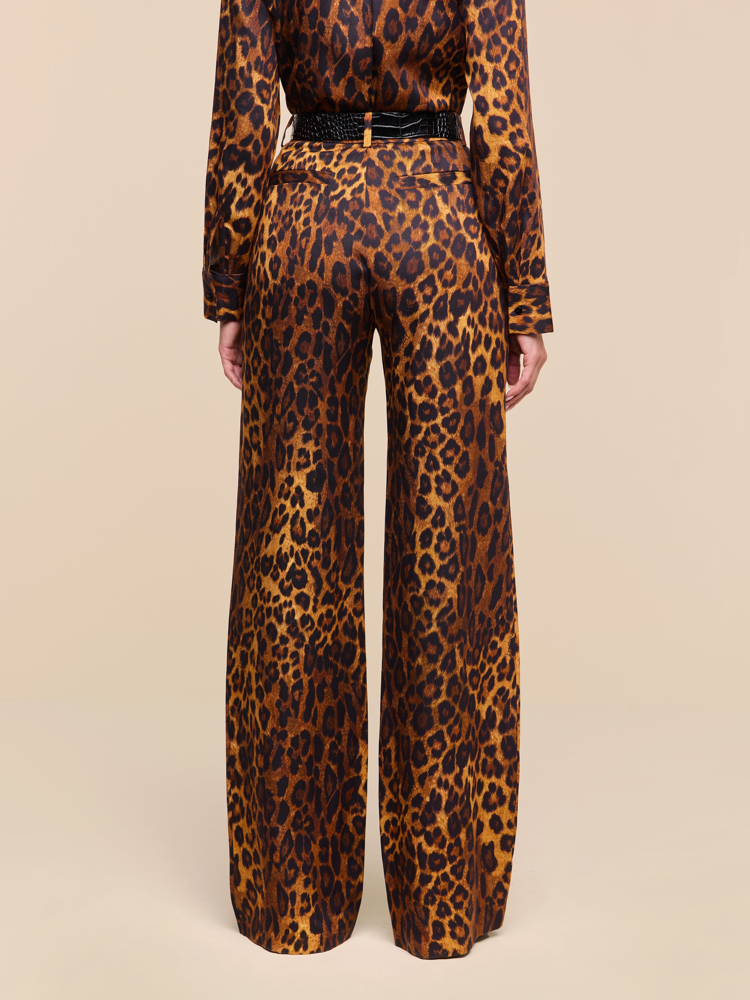 A person stands with their back to the camera, wearing the Livvy Trouser and a matching long-sleeve top in a tan leopard print pattern against a plain white background.