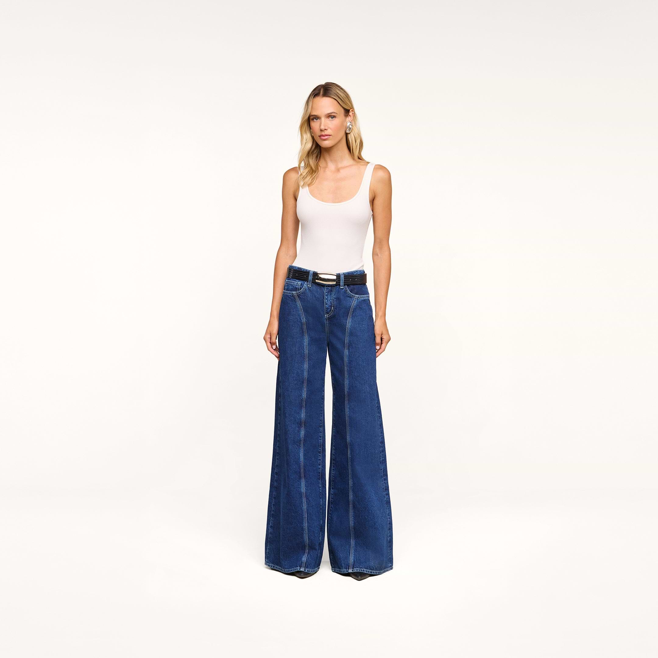 Wearing the Lestat Wide-Leg Jean, a woman in a white tank top stands against a plain white background.