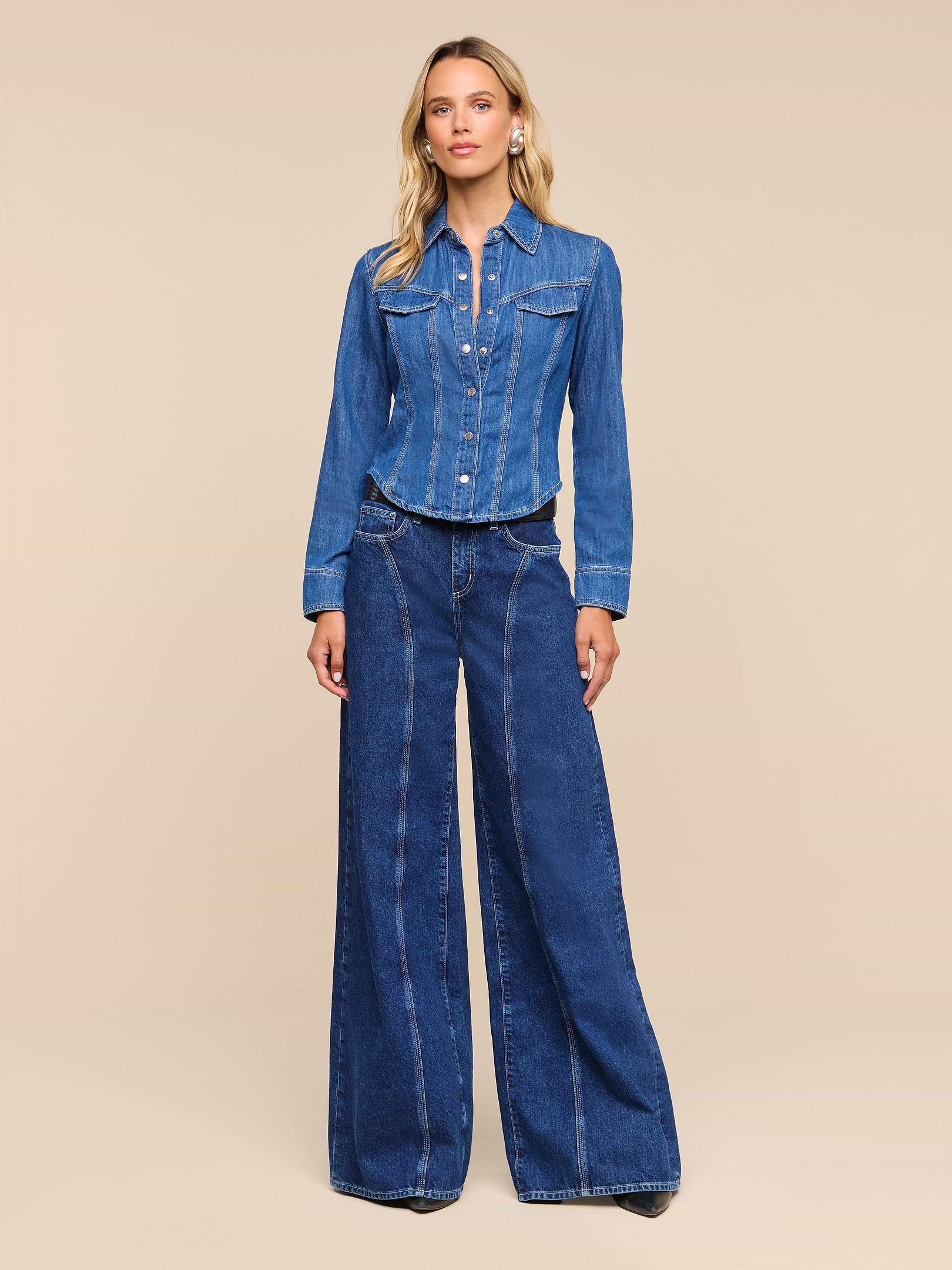 A woman stands against a white background wearing an all-cotton denim jacket and the Lestat Wide-Leg Jean, looking straight ahead with a relaxed expression.