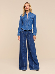 A woman stands against a white background wearing an all-cotton denim jacket and the Lestat Wide-Leg Jean, looking straight ahead with a relaxed expression.