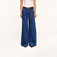 A model, shown from the shoulders down and standing against a plain white background, wears the Lestat Wide-Leg Jean—a high-rise, wide-leg style crafted from all-cotton denim—paired with a white sleeveless top and black belt.