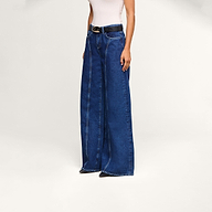 A person wearing the Lestat Wide-Leg Jean—a high-rise, wide-leg style made from all-cotton blue denim—along with a sleeveless white top and a black belt stands against a plain light background. Their face is not visible in the image.