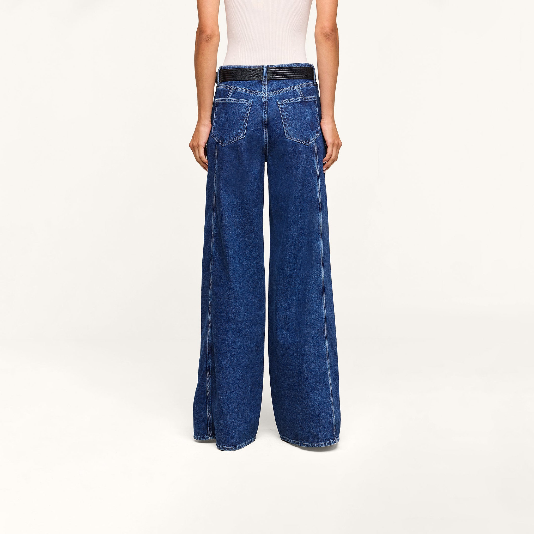 A person is shown from the back against a plain light background, wearing the Lestat Wide-Leg Jean in dark blue all-cotton denim and a white sleeveless top.