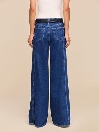 Model showcases the Lestat Wide-Leg Jean—a pair of high-rise, wide-leg blue jeans crafted from 100 cotton denim and featuring two back pockets—styled with a white sleeveless top and black belt, photographed from the back against a plain beige background.