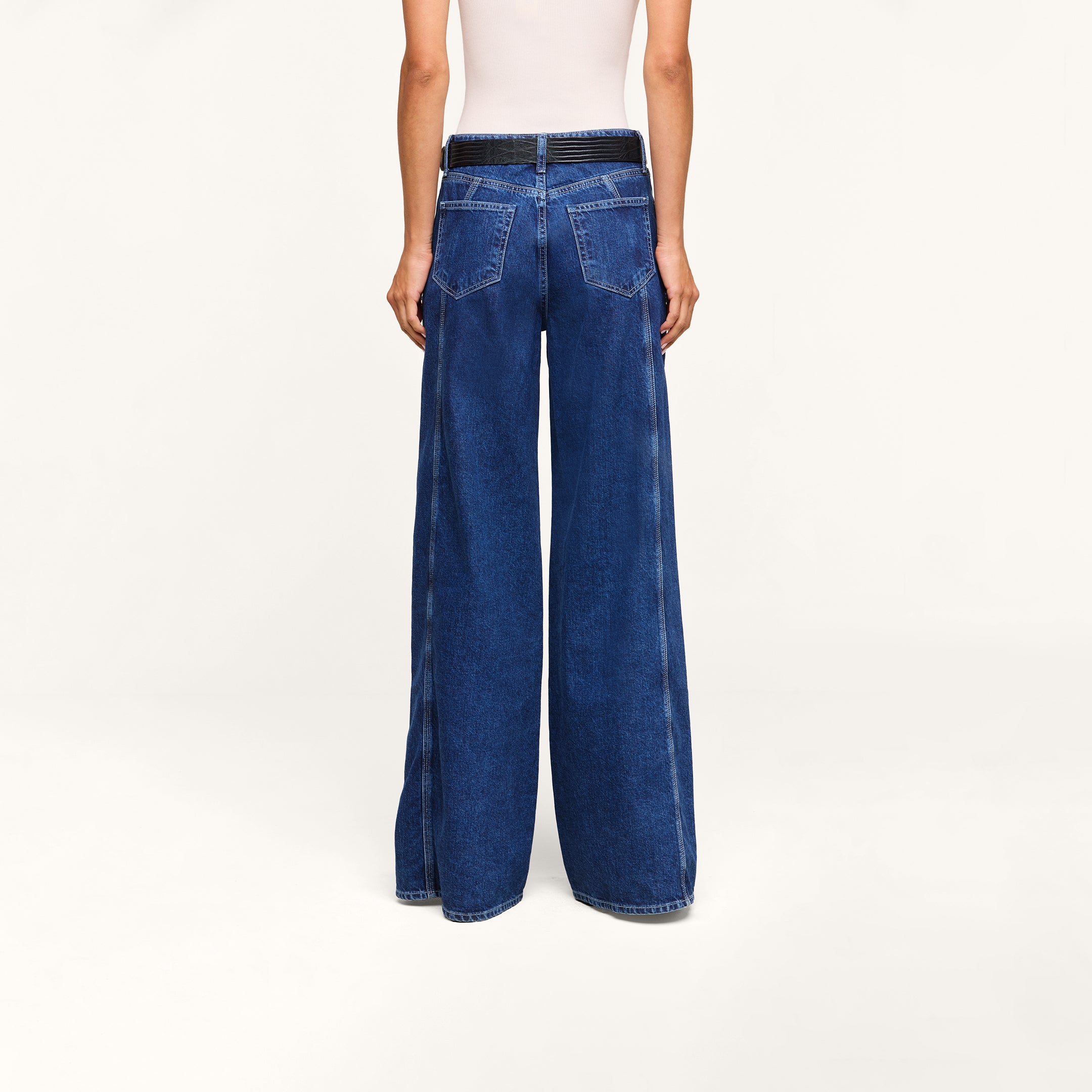 A person is shown from the back against a plain light background, wearing the Lestat Wide-Leg Jean in dark blue all-cotton denim and a white sleeveless top.